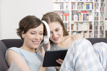 Mother and adult daughter with sharing digital tablet and headphones - FMKF002419