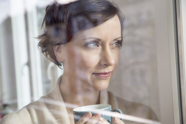 Frau hält Tasse und schaut aus dem Fenster - FMKF002421