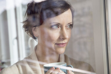 Woman holding cup looking out of window - FMKF002421