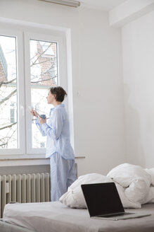 Frau im Schlafzimmer schaut aus dem Fenster - FMKF002433