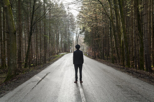 Deutschland, Rückenansicht eines jungen, schwarz gekleideten Mannes auf einer leeren Landstraße - TCF004934