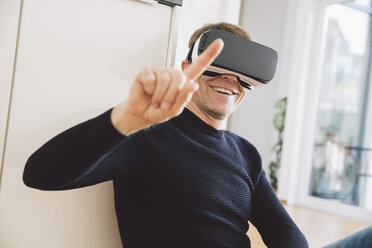 Smiling man wearing virtual reality glasses pointing his finger - MFF002733