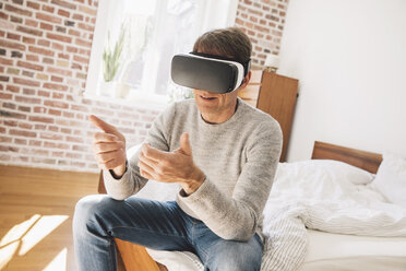 Mann sitzt auf dem Bett und trägt eine Virtual-Reality-Brille - MFF002736