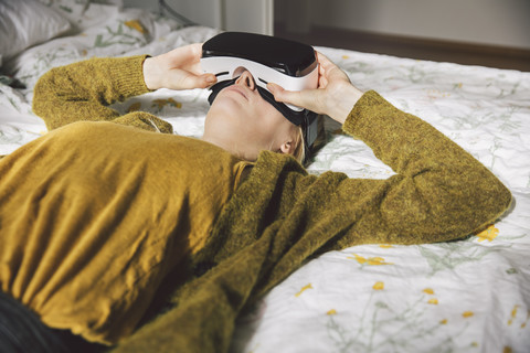 Frau mit Virtual-Reality-Brille auf dem Bett liegend, lizenzfreies Stockfoto