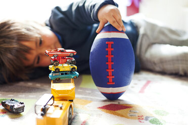 Junge auf dem Boden liegend mit Fußball und Stapel von Spielzeugautos - VABF000269