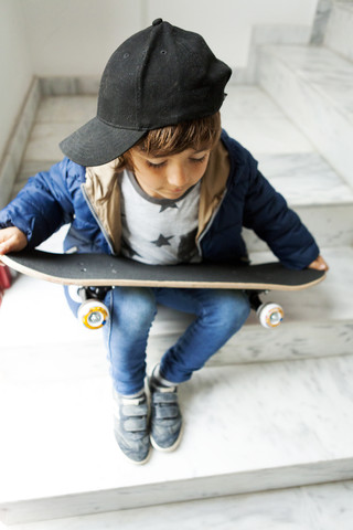 Junge sitzt auf einer Treppe und hält ein Skateboard, lizenzfreies Stockfoto