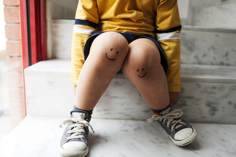 Boy sitting on stairs with smiley faces on his knees stock photo