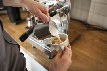 Cappuccino, Mann gießt Milchschaum in Kaffeetasse - PAF001568