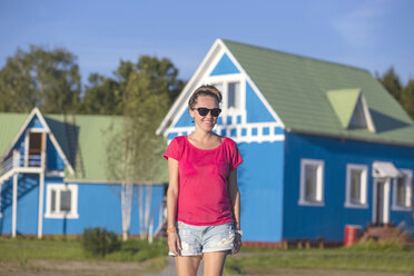 Smiling young woman with blue housee in background - KNTF000241