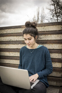 Teenager-Mädchen sitzt im Freien und benutzt einen Laptop - EGBF000134