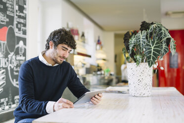 Junger Mann in einem Café mit Blick auf ein digitales Tablet - ALBF000025