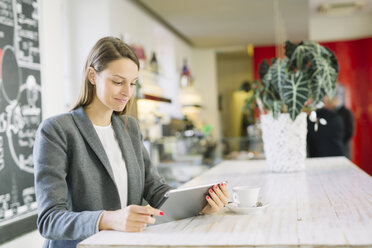 Junge Frau in einem Café mit Blick auf ein digitales Tablet - ALBF000030