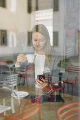 Junge Frau in einem Café schaut auf ihr Handy - ALBF000032