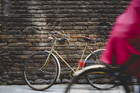 Vintage bicycle leaning against a brick wall while cyclist passing by - GIOF000787