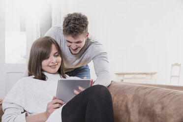 Glückliches junges Paar zu Hause, das sich ein digitales Tablet teilt - FMKF002437