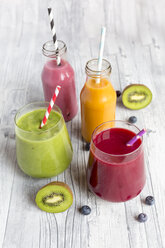 Glasses of four different smoothies and fruits on wood - SARF002612
