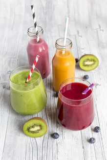 Glasses of four different smoothies and fruits on wood - SARF002612