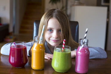 Portrait of smiling girl sitting at table with four different smoothies at choice - SARF002613