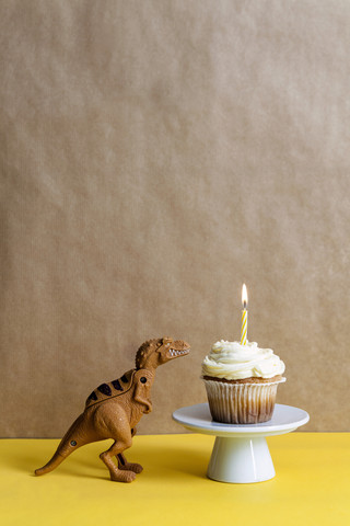 Spielzeug-Dinosaurier und Tassenkuchen mit brennenden Kerzen auf einem Tortenständer, lizenzfreies Stockfoto