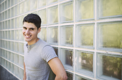 Porträt eines lächelnden jungen Mannes, der vor einer Wand steht - RAEF000920