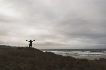 France, Bretagne, Finistere, Crozon peninsula, man standing at the coast under cloudy sky spreading out his arms - UUF006649