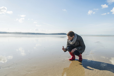 Frankreich, Bretagne, Finistere, Halbinsel Crozon, Frau findet eine Muschel am Strand, lizenzfreies Stockfoto