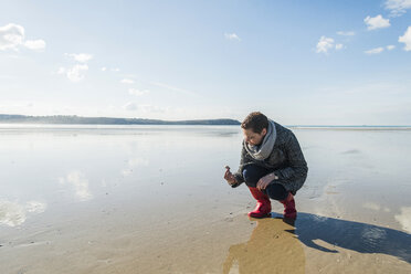 Frankreich, Bretagne, Finistere, Halbinsel Crozon, Frau findet eine Muschel am Strand - UUF006662
