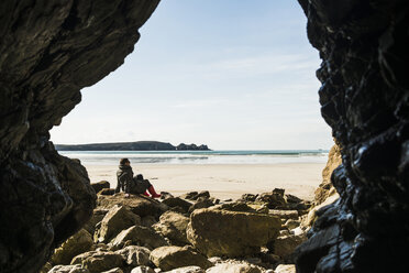 Frankreich, Bretagne, Finistere, Halbinsel Crozon, Frau am Strand sitzend von Felshöhle aus gesehen - UUF006673