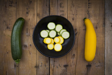 Yellow and green zucchini and bowl of zucchini slices on wood - LVF004610