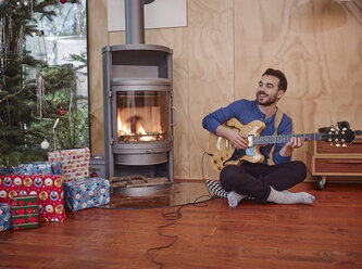 Mann sitzt auf dem Boden und spielt E-Gitarre am Weihnachtsbaum - RHF001306