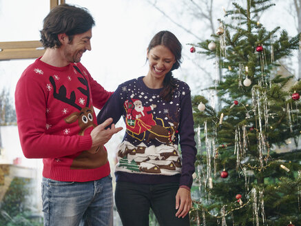 Ein Paar steht vor einem Weihnachtsbaum und trägt Weihnachtspullis - RHF001319