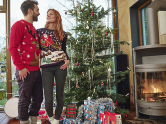 Glückliches Paar vor dem Weihnachtsbaum in Weihnachtspullis - RHF001331