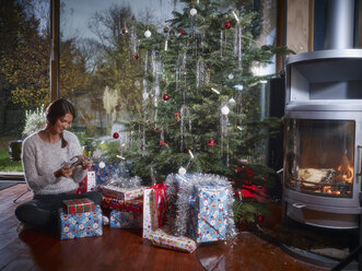 Woman unwrapping Christmas gifts under Christmas tree - RHF001336