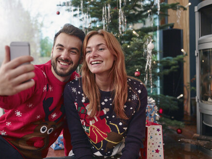 Happy couple taking selfie in front of Christmas tree - RHF001341