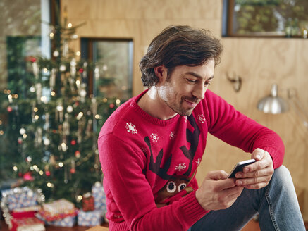 Mann benutzt Smartphone vor einem Weihnachtsbaum - RHF001343