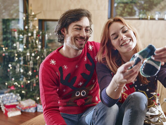 Glückliches Paar packt vor dem Weihnachtsbaum Kinderschuhe aus - RHF001346