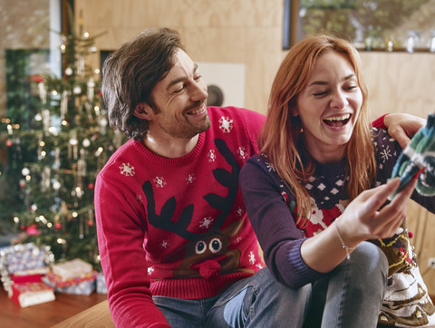 Glückliches Paar packt vor dem Weihnachtsbaum Kinderschuhe aus, lizenzfreies Stockfoto