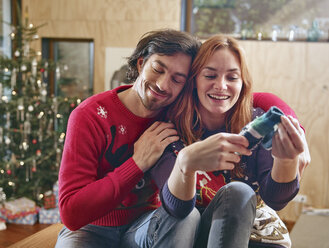 Glückliches Paar packt vor dem Weihnachtsbaum Kinderschuhe aus - RHF001348