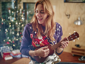 Blonde Frau spielt Ukulele vor einem Weihnachtsbaum - RHF001350