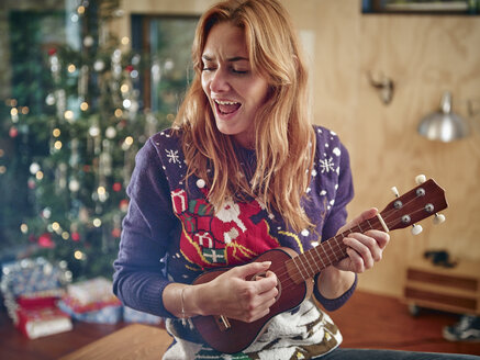 Blond woman playing ukulele in front of Christmas tree - RHF001350