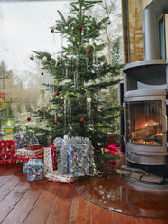 Christmas presents under Christmas tree next to cozy fireplace - RHF001356