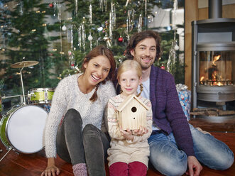Eltern sitzen mit Tochter vor dem Weihnachtsbaum und lächeln - RHF001363