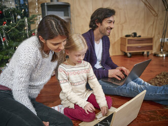 Father using laptop, mother playing with daughter on toy computer on Christmas Eve - RHF001364