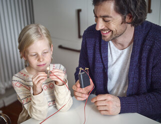 Vater erklärt seiner Tochter den Stromkreislauf mit der Batterie und dem Akku - RHF001369