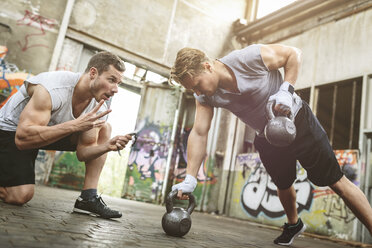 Young man having a workout with kettlebells supported by training partner - MADF000850