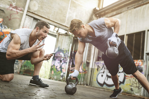 Junger Mann beim Training mit Kettlebells, unterstützt von einem Trainingspartner - MADF000850