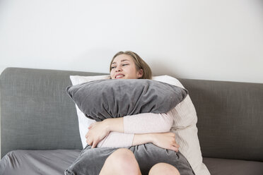 Happy young woman lying on her bed hugging pillow - FMKF002457