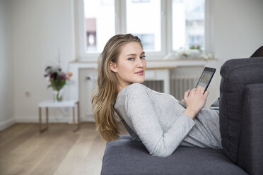 Portrait of young woman lying on couch with digital tablet - FMKF002468