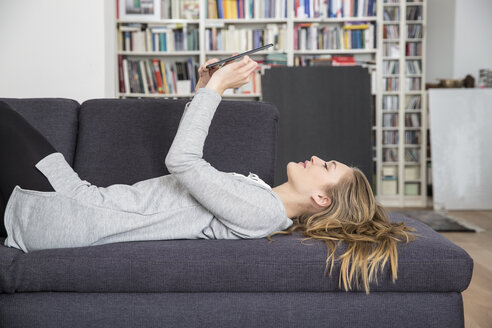 Junge Frau auf der Couch liegend mit digitalem Tablet - FMKF002472