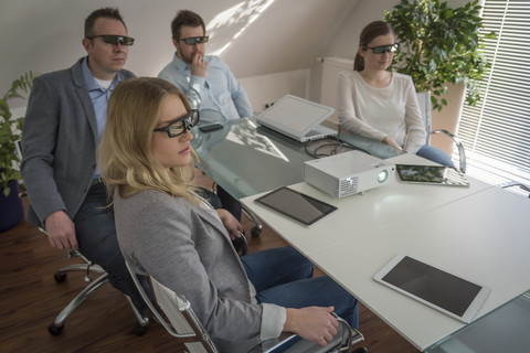Vier Kollegen mit 3D-Brillen bei einer Präsentation mit Projektor im Konferenzraum, lizenzfreies Stockfoto